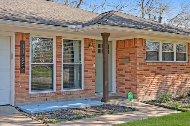 doorway to property featuring a shingled roof, brick siding, and a garage