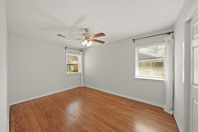 empty room with ceiling fan, wood finished floors, visible vents, and baseboards