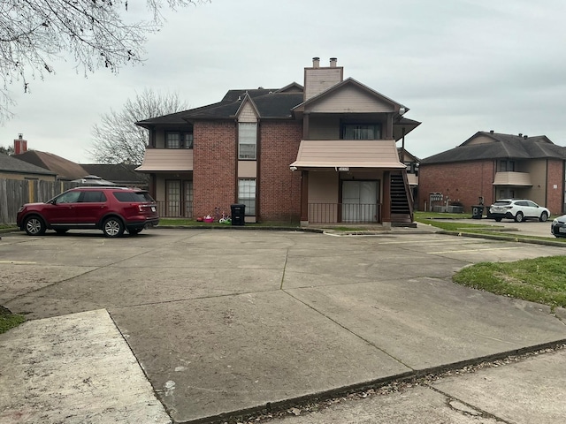 view of front of house featuring uncovered parking, brick siding, a chimney, and stairs