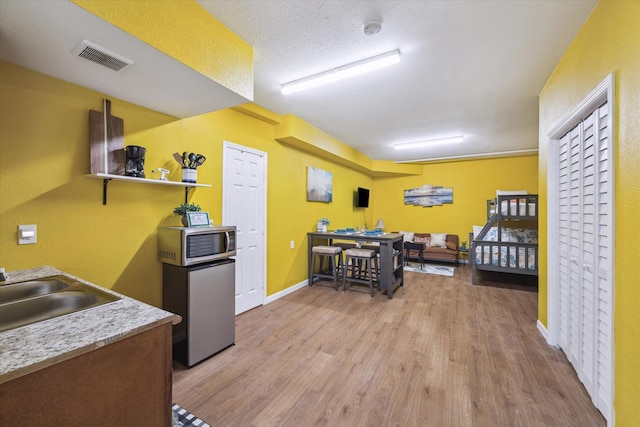 kitchen featuring light countertops, stainless steel microwave, light wood-style flooring, visible vents, and a sink