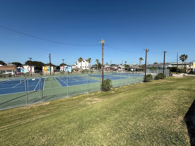 view of tennis court with a residential view, a lawn, and fence