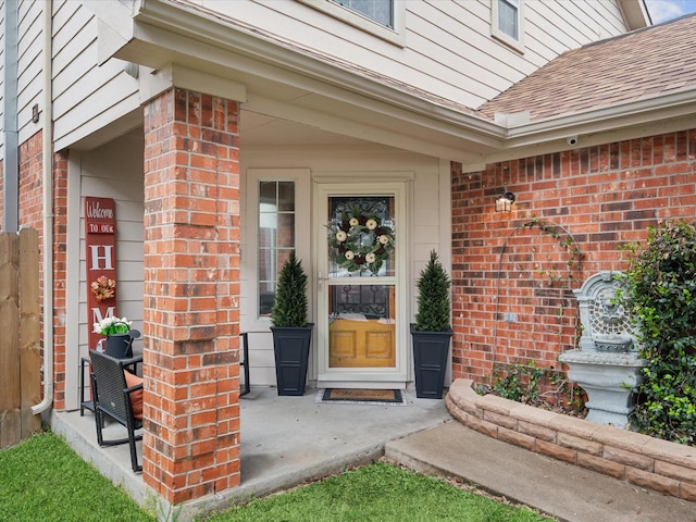 property entrance featuring brick siding and a shingled roof