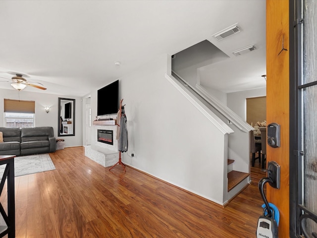 living room with a glass covered fireplace, visible vents, wood finished floors, and stairway