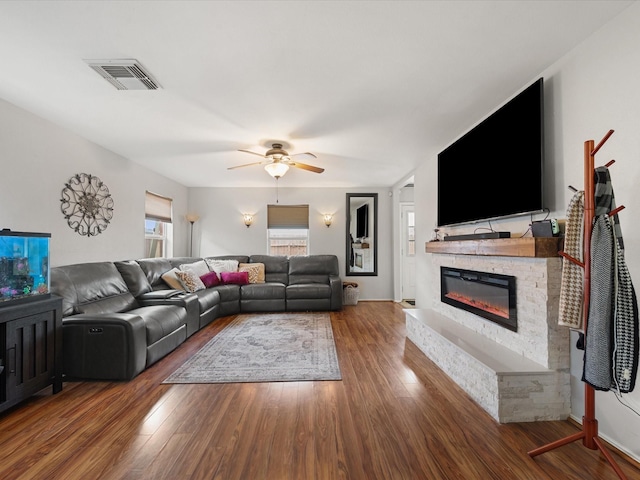 living room with a fireplace, wood finished floors, visible vents, and ceiling fan