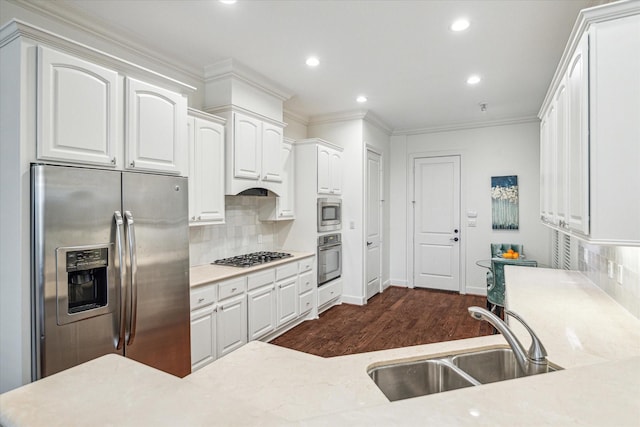 kitchen with appliances with stainless steel finishes, dark wood-type flooring, ornamental molding, white cabinetry, and a sink