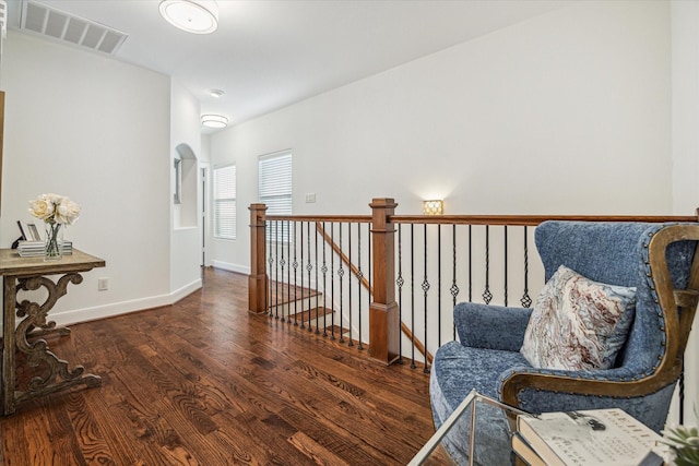 corridor with dark wood-style floors, arched walkways, visible vents, an upstairs landing, and baseboards