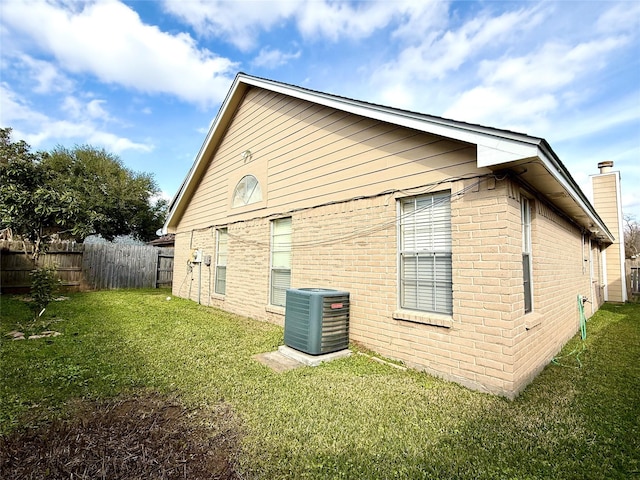 view of side of home featuring a yard, brick siding, cooling unit, and fence