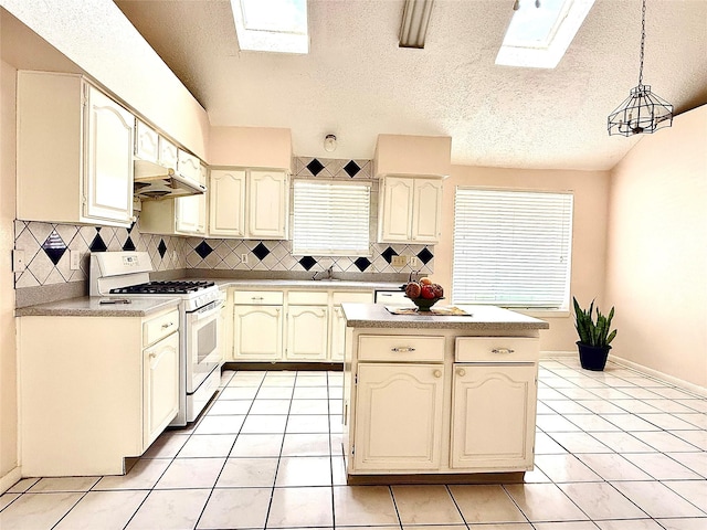 kitchen with a skylight, pendant lighting, white gas stove, light countertops, and under cabinet range hood