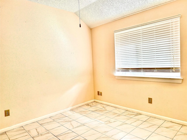 unfurnished room with vaulted ceiling, a textured ceiling, and baseboards