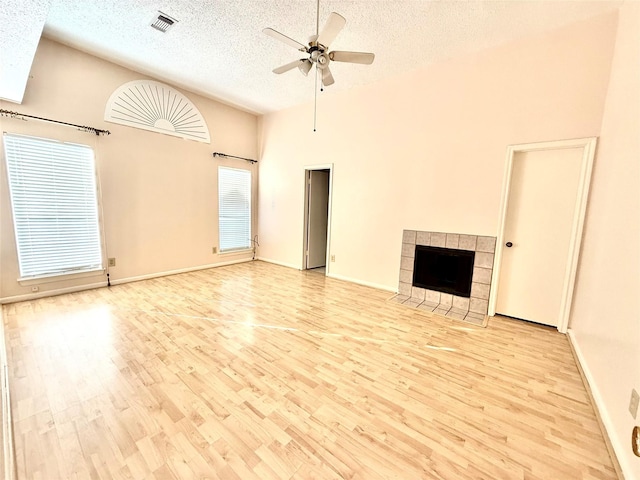 unfurnished living room with ceiling fan, a textured ceiling, light wood-style flooring, visible vents, and a tiled fireplace