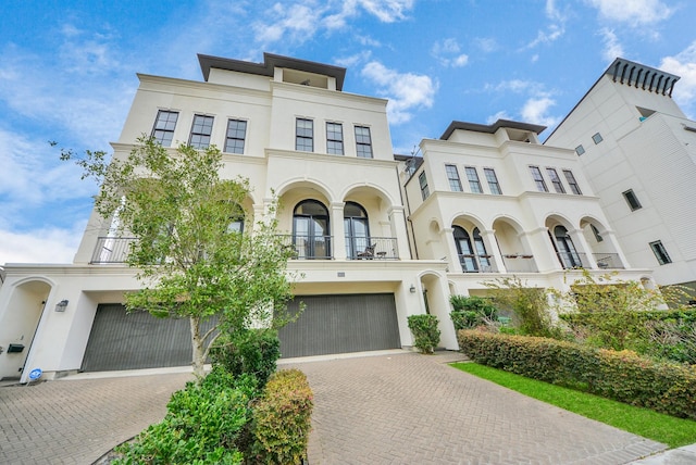 multi unit property with a garage, driveway, a balcony, and stucco siding