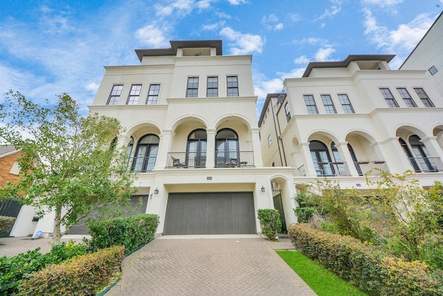 view of front of house featuring decorative driveway, french doors, stucco siding, a balcony, and a garage