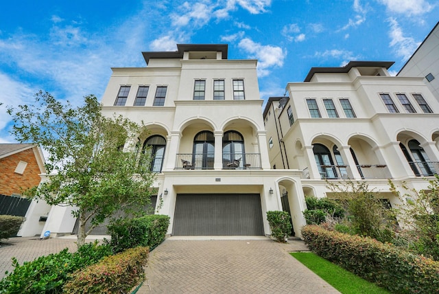 view of front of property featuring a garage, decorative driveway, a balcony, and stucco siding