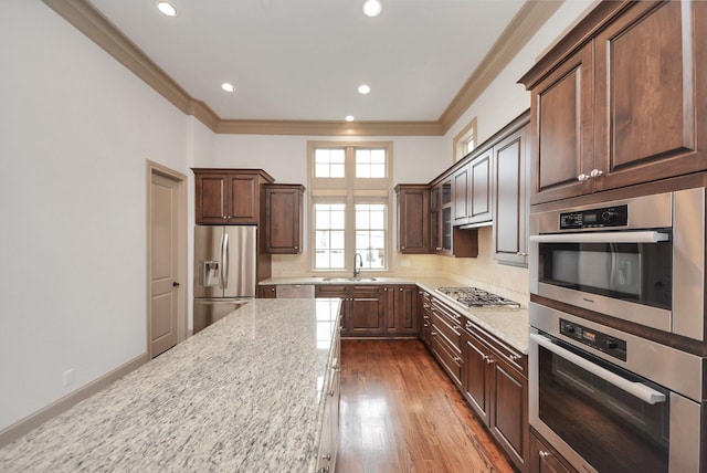 kitchen featuring dark wood finished floors, appliances with stainless steel finishes, light stone countertops, crown molding, and a sink