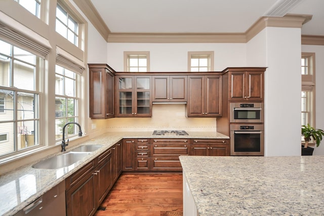 kitchen featuring light stone counters, stainless steel appliances, a sink, light wood-style floors, and ornamental molding