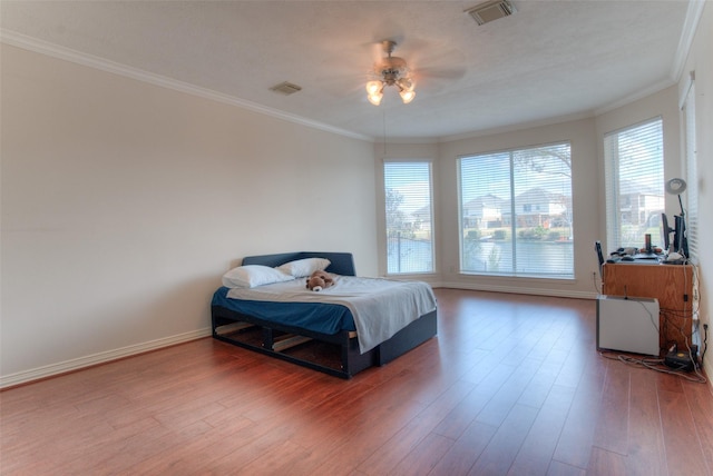 bedroom featuring ornamental molding, visible vents, baseboards, and wood finished floors