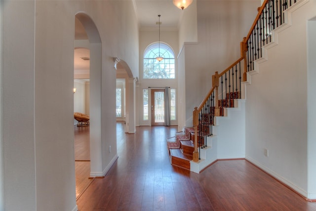 entrance foyer with baseboards, arched walkways, ornamental molding, wood finished floors, and a high ceiling