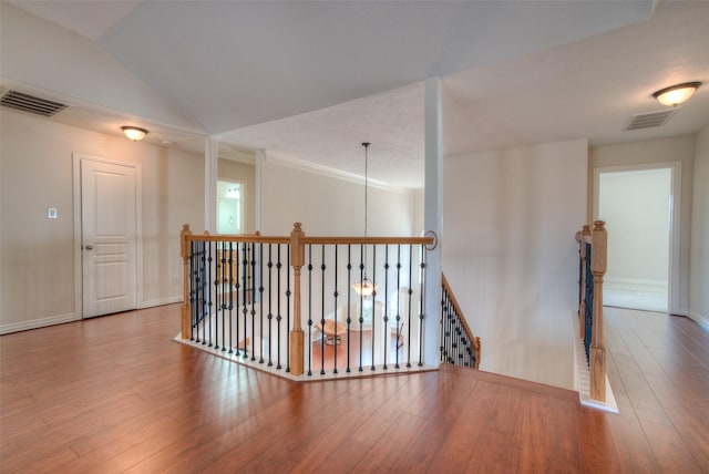 corridor featuring lofted ceiling, visible vents, an upstairs landing, and wood finished floors