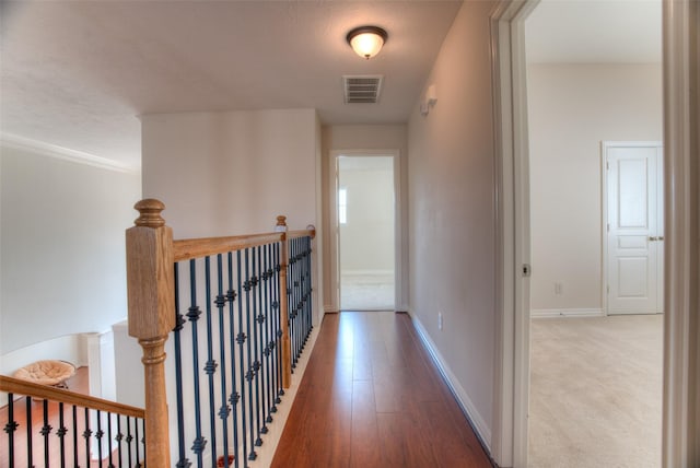 hallway with baseboards, visible vents, an upstairs landing, and wood finished floors