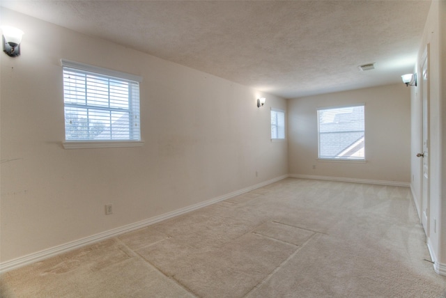 spare room featuring a textured ceiling, baseboards, visible vents, and light colored carpet