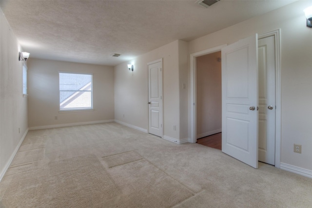 empty room featuring light carpet, baseboards, and a textured ceiling