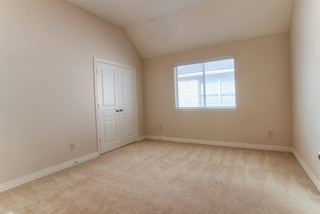 empty room featuring light carpet, vaulted ceiling, and baseboards