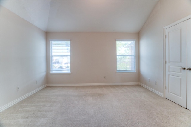 spare room featuring lofted ceiling, light colored carpet, and baseboards