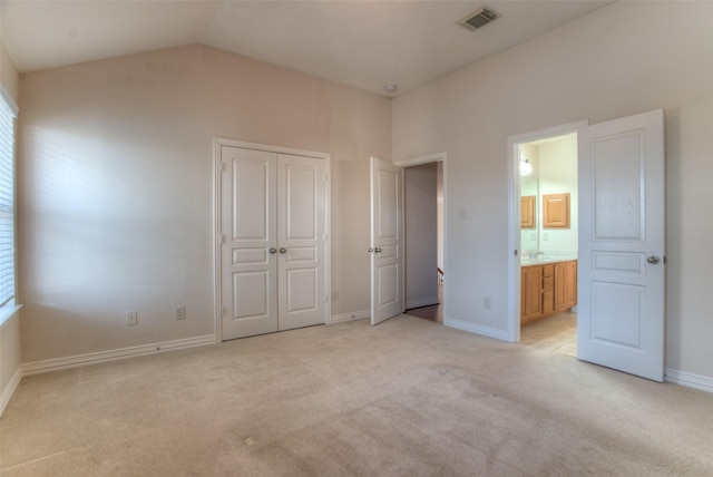 unfurnished bedroom featuring light carpet, baseboards, visible vents, lofted ceiling, and ensuite bathroom