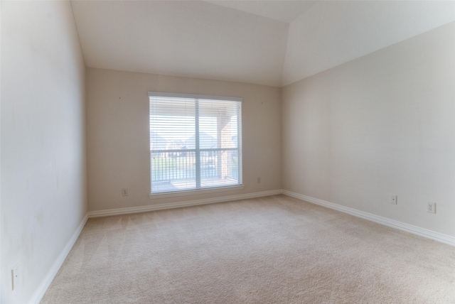 spare room with light colored carpet, vaulted ceiling, and baseboards