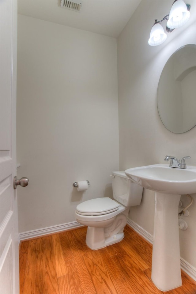 half bath with baseboards, visible vents, toilet, and wood finished floors