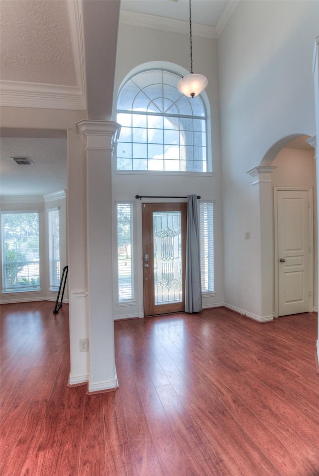 entrance foyer featuring ornate columns, visible vents, ornamental molding, and wood finished floors