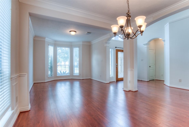 spare room featuring arched walkways, wood finished floors, decorative columns, and crown molding