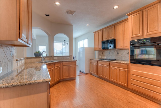 kitchen with light wood-style flooring, a peninsula, a sink, visible vents, and black appliances