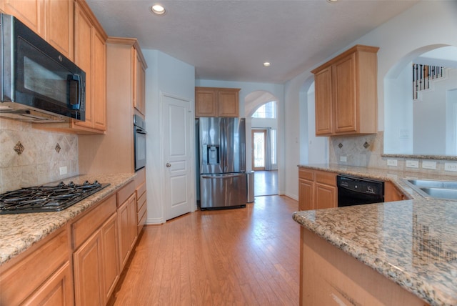 kitchen featuring light stone counters, arched walkways, backsplash, light wood-style flooring, and black appliances