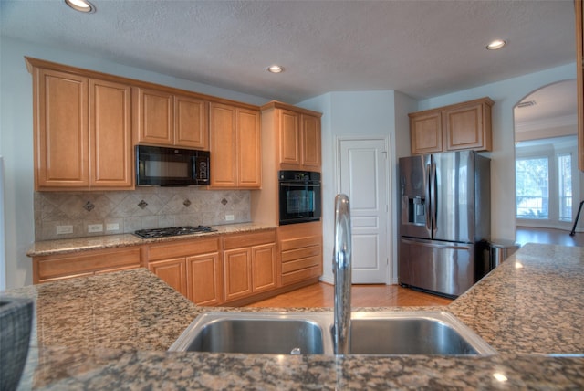 kitchen with light stone counters, arched walkways, backsplash, a sink, and black appliances