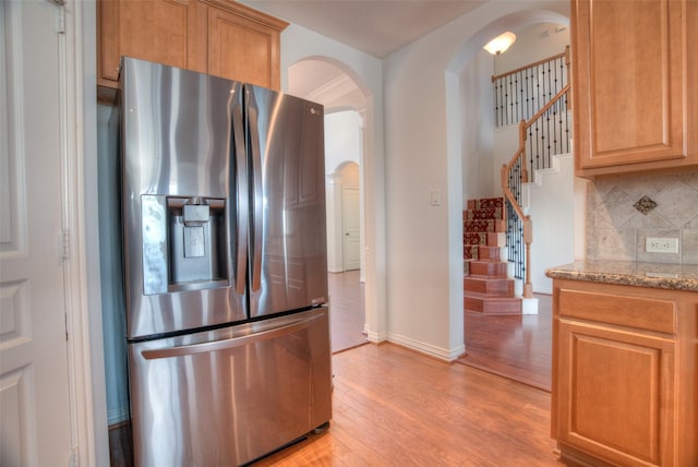 kitchen with arched walkways, light stone countertops, light wood-style floors, stainless steel refrigerator with ice dispenser, and decorative backsplash