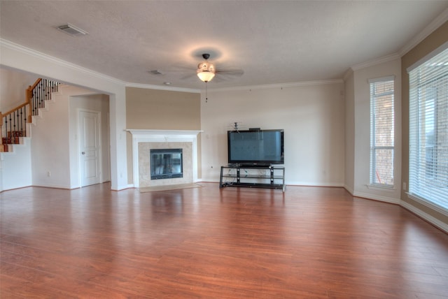 unfurnished living room featuring dark wood-type flooring, a tile fireplace, a ceiling fan, and crown molding