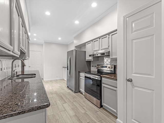 kitchen with under cabinet range hood, stainless steel appliances, wood finish floors, a sink, and ornamental molding