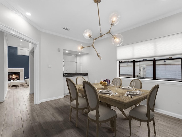 dining area featuring baseboards, a tile fireplace, wood finished floors, and crown molding