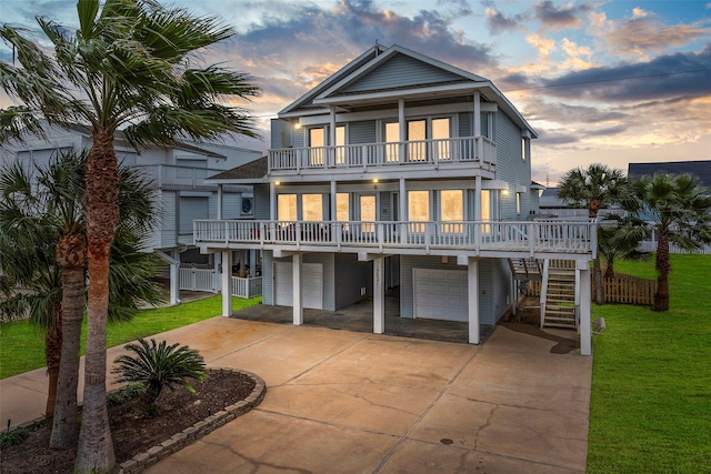 rear view of house featuring an attached garage, a balcony, stairs, a yard, and concrete driveway