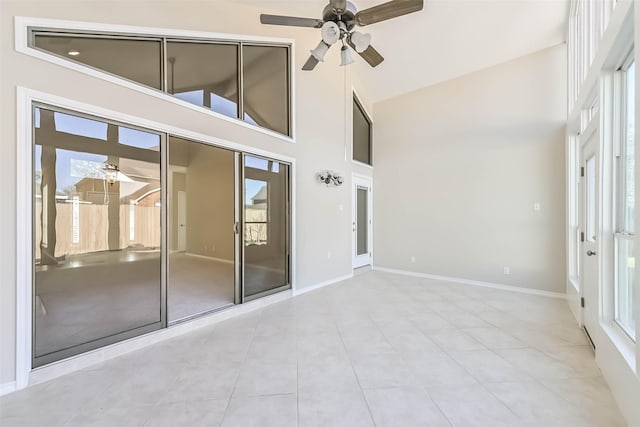 interior space featuring baseboards, a high ceiling, a ceiling fan, and a healthy amount of sunlight