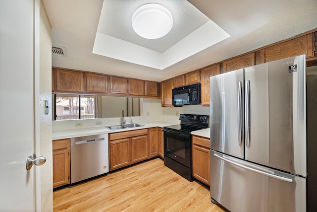 kitchen featuring light wood finished floors, black appliances, a sink, a tray ceiling, and light countertops