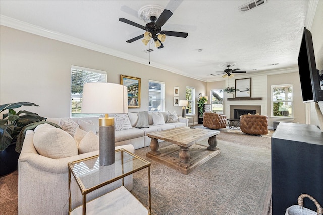 living area with a large fireplace, visible vents, a ceiling fan, ornamental molding, and carpet flooring