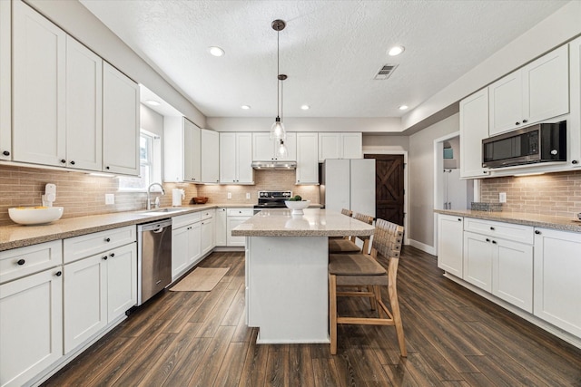 kitchen with hanging light fixtures, appliances with stainless steel finishes, a sink, and white cabinetry