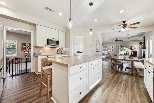 kitchen featuring visible vents, white cabinets, stainless steel microwave, open floor plan, and decorative light fixtures