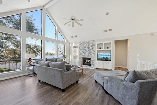 living room featuring built in shelves, beam ceiling, visible vents, a large fireplace, and wood finished floors