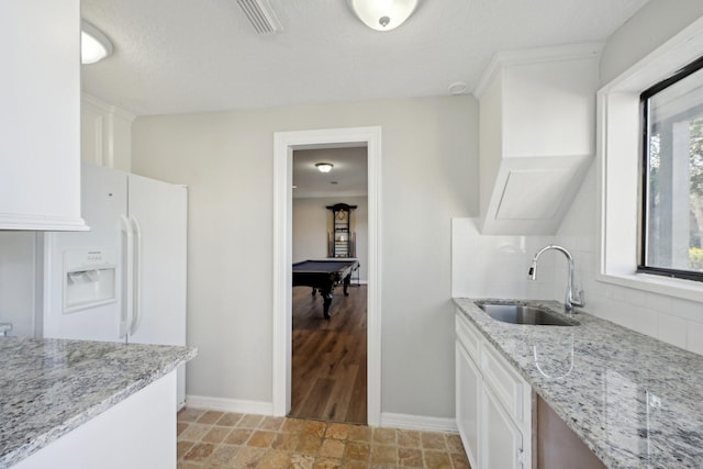 kitchen with light stone counters, pool table, a sink, white cabinetry, and backsplash