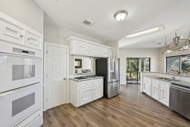 kitchen featuring stainless steel appliances, visible vents, white cabinets, a sink, and wood finished floors