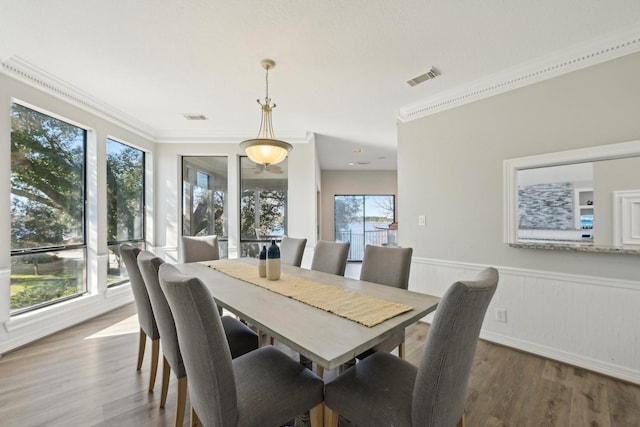 dining area featuring a wainscoted wall, crown molding, visible vents, and wood finished floors