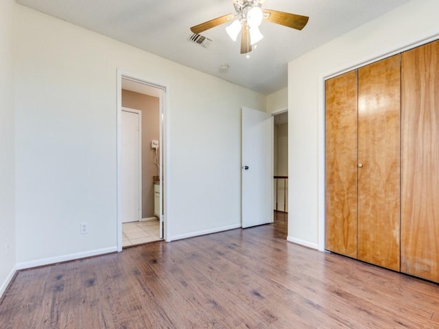 unfurnished bedroom featuring baseboards, visible vents, ensuite bath, wood finished floors, and a closet